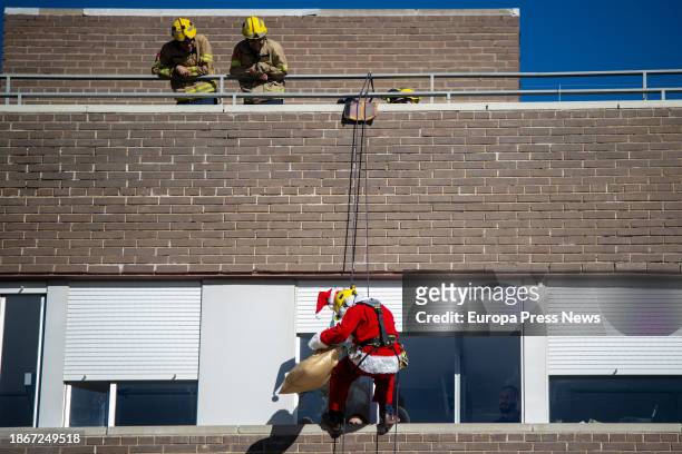 Firefighters help Santa Claus to zip-line down the facade of the Germans Trias Hospital to greet pediatric patients on December 19 in Badalona,...