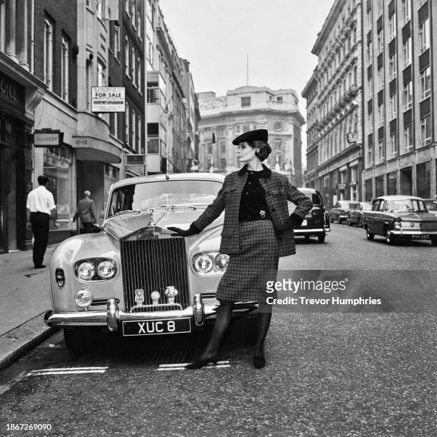 Model Alexis Drury, wearing a black-and-beige Christian Dior hunting suit, trimmed with black velvet, poses beside a Rolls-Royce Phantom V Limousine,...