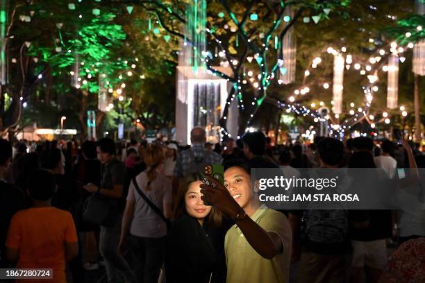 People take a selfie during a Christmas light show ahead of festivities at a park in Makati, Metro Manila on December 22, 2023.