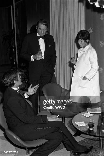 Actor Omar Sharif wearing a tuxedo talking to actor Gregory Peck and a model at a party for Andre Courreges at his Los Angeles factory