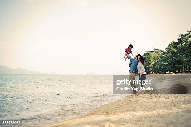 parents lifting daughter mid air on beach - japanese couple beach stock-fotos und bilder