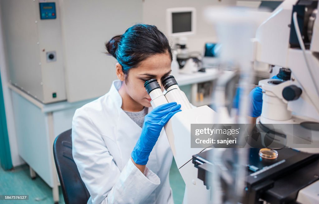 Mujer científica trabajando en el laboratorio, usando el microscopio
