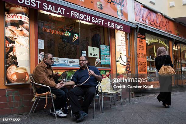 El Mohamed smokes a hookah pipe as he talks with native Palestinian Yaser A Rabah in front of a bar at Sonnenallee in Neukoelln district on October...
