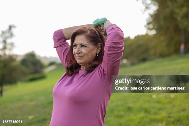 overweight senior woman does exercise in the park, curvy with small dumbbells cardio workout - voluptuous stock pictures, royalty-free photos & images