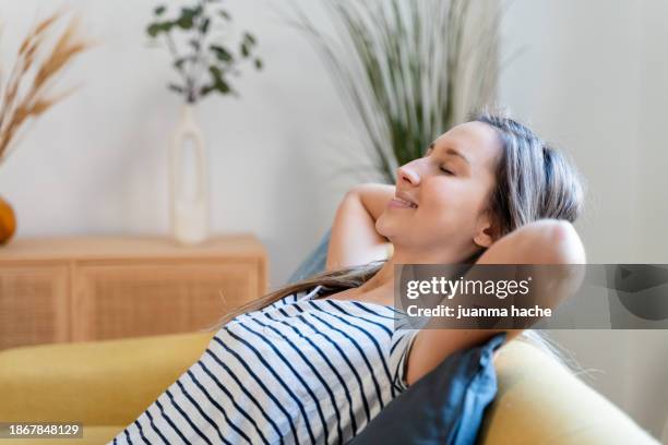 portrait of a smiling young woman relaxing on a sofa at home - lawn aeration stock pictures, royalty-free photos & images