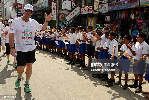 In this handout image provided by Laureus, Sir Ian Botham waves to children lining the street during the fourth day of Beefy's Big Sri Lanka walk...