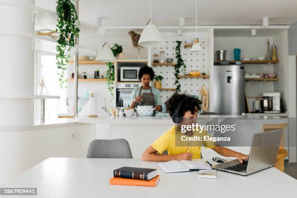boy doing homework while his mother cooking in the background - parents and teenagers stock pictures, royalty-free photos & images