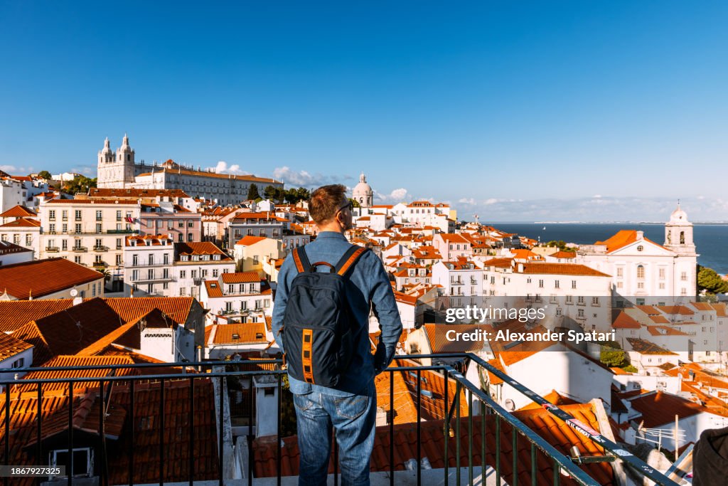 Man with backpack looking at Lisbon old town cityscape from a scenic viewpoint (miradouro), Portugal