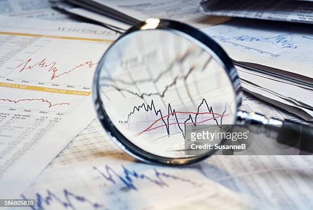 magnifying glass on top of financial market info - magnifying glass stock pictures, royalty-free photos & images