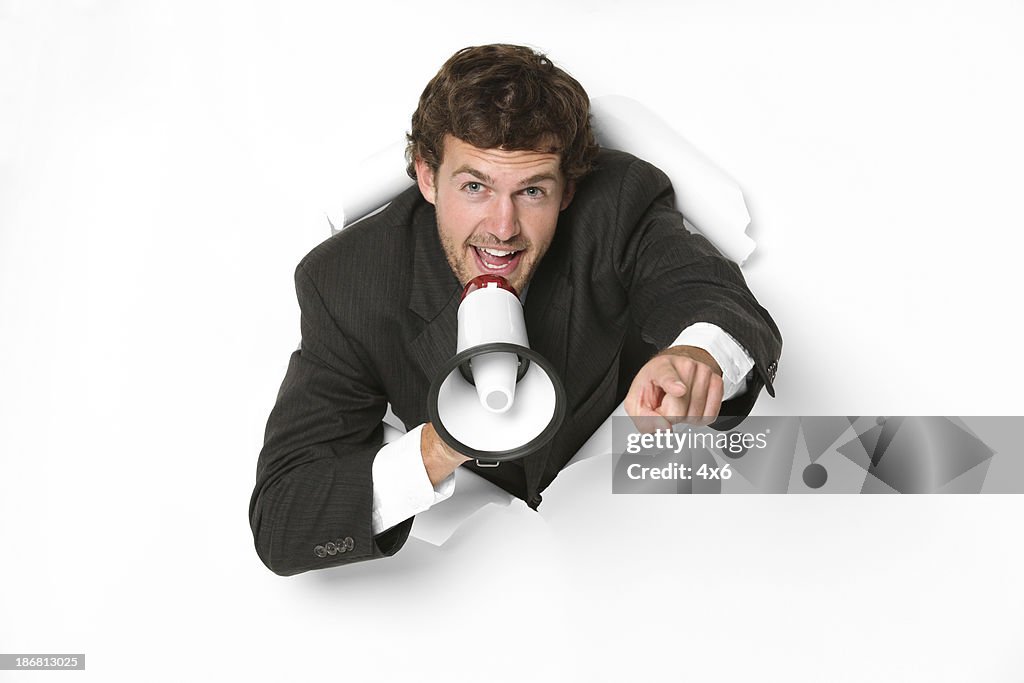 Businessman emerging through a hole and shouting into megaphone