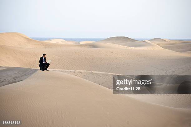 man working on laptop sitting on a sandy desert hill - remote location stock pictures, royalty-free photos & images