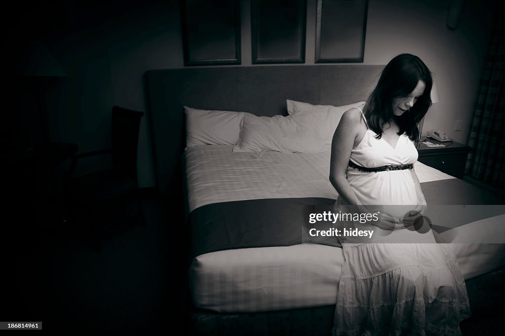A black and white photo of a pregnant woman sat on the bed