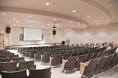 Empty lecture hall with several rows of seats and a screen