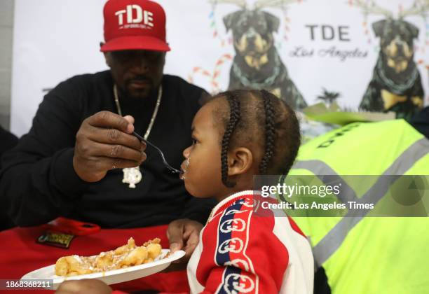 Watts, Los Angeles, CA Founder and CEO of Top Dawg Entertainment Anthony Tiffith gives funnel cake to Saint during a toy giveaway sponsored by Top...