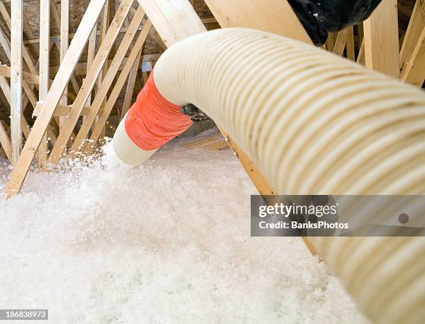 worker spraying blown fiberglass insulation between attic trusses - insulator stock pictures, royalty-free photos & images