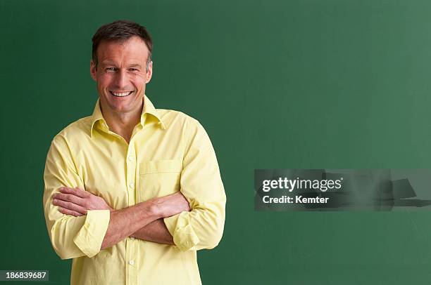 a smiling teacher with arms crossed in front of chalkboard - green shirt stock pictures, royalty-free photos & images