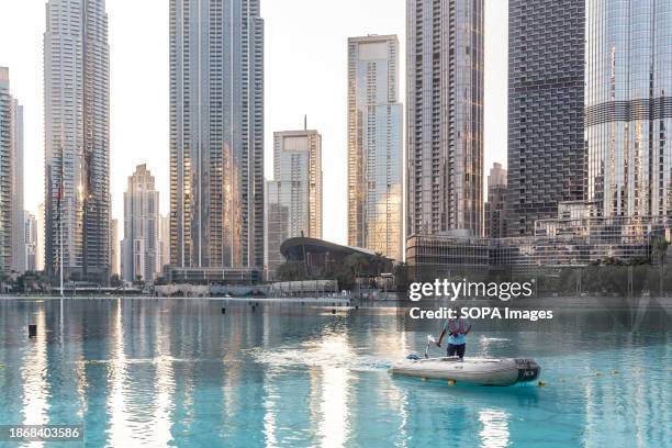 Man rides a boat on the waters of the Dubai Fountain with modern architecture buildings in the background.