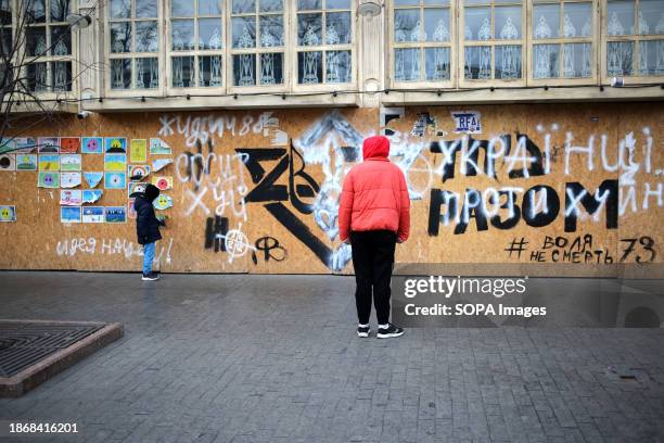 An adult and a child stand near anti-semitic inscriptions reading "Ukrainians are against bullshit" and "Jews suck dick 1488" on Deribasovskaya...