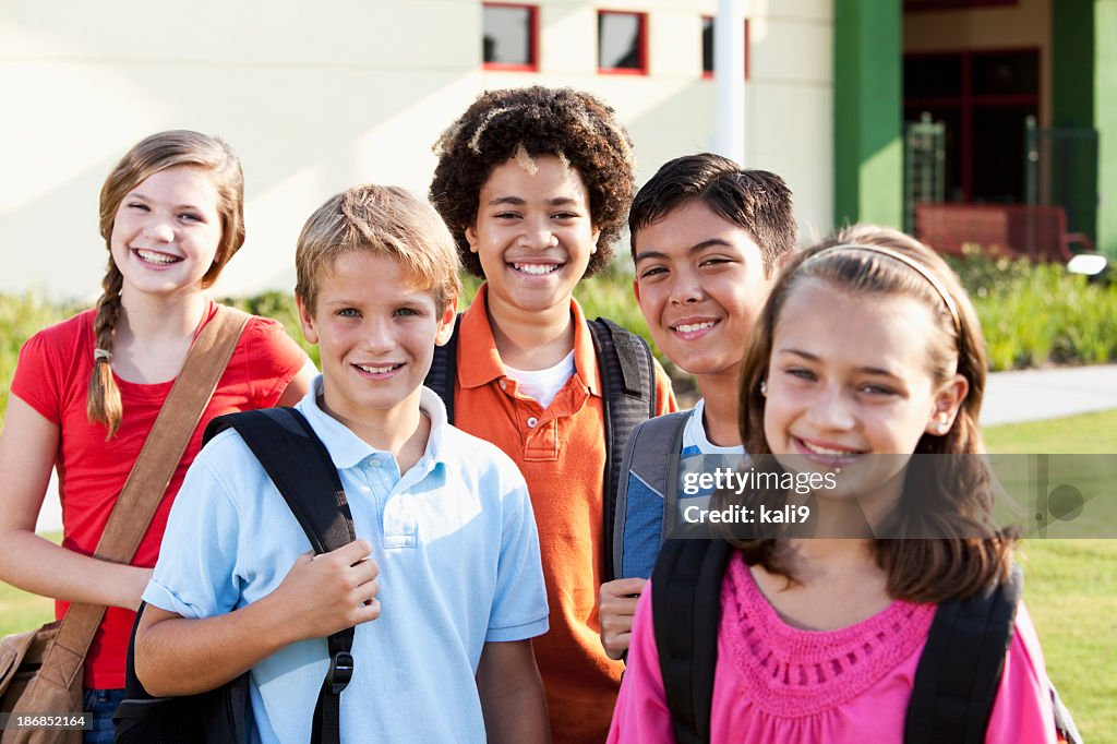 Happy children standing outside school with bookbags
