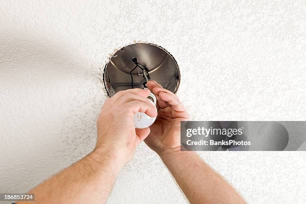 electrician installs 100w light bulb into a new recessed fixture - installing ceiling light fixture stock pictures, royalty-free photos & images