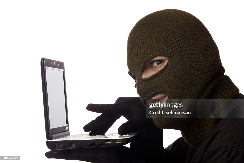 Young man wearing snow mask and posing as computer hacker