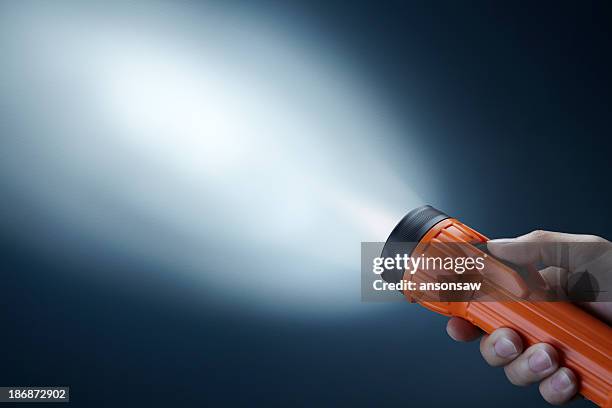 person holdings orange flashlight searching in darkness - flashlight stock pictures, royalty-free photos & images