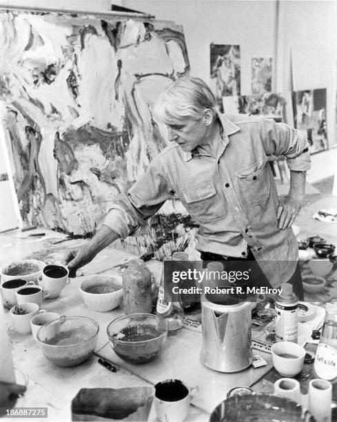 The painter Willem de Kooning mixes paints in his studio, surrounded by his abstract paintings, Long Island, New York, 1967.