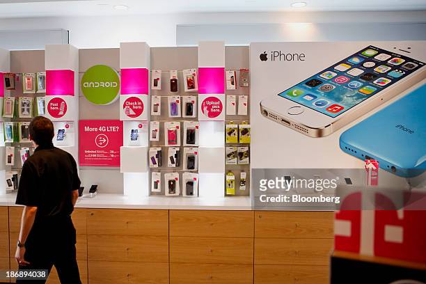 An employee walks past an Apple Inc. IPhone advertisement to help a customer find an accessory at a T-Mobile US Inc. Retail store in Torrance,...