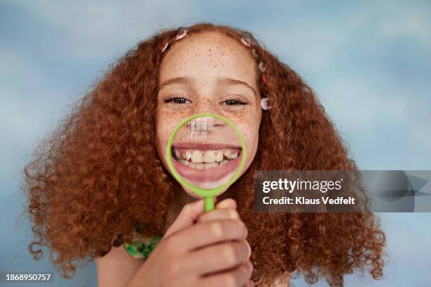 happy redhead girl holding magnifying glass over mouth - poner caras fotografías e imágenes de stock