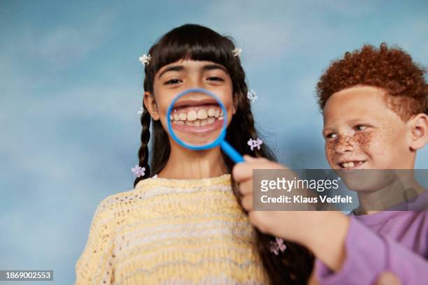 smiling boy holding magnifying glass over friend's teeth - tooth bonding stock pictures, royalty-free photos & images