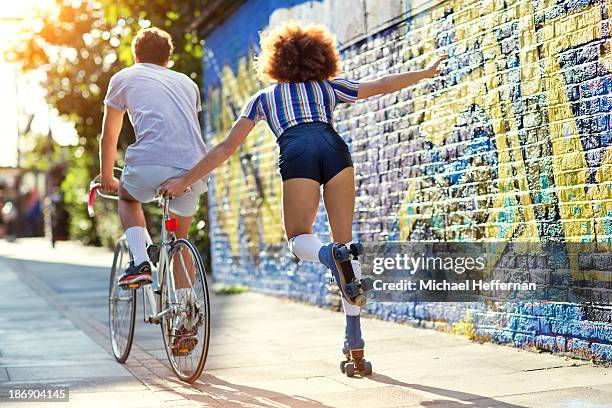 man on bike towing young woman on rollerskates - woman sleep stockfoto's en -beelden