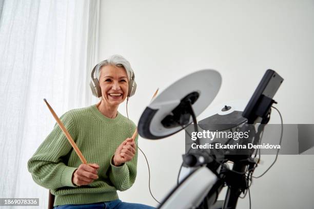 cheerful senior woman playing drums - musikinstrument stock-fotos und bilder