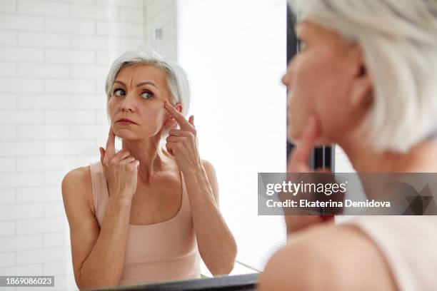 elderly woman examining face in mirror - wrinkled stock pictures, royalty-free photos & images
