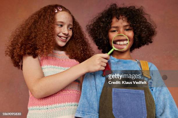 girl holding magnifying glass over boy's mouth - tooth bonding stock pictures, royalty-free photos & images