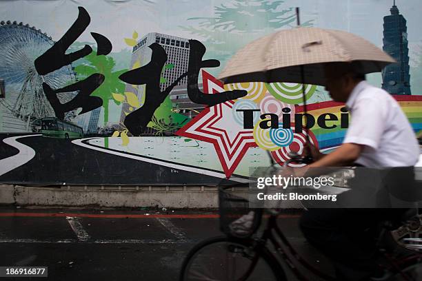 Man holding an umbrella cycles past a tourism advertisement for Taipei in Taipei, Taiwan, on Monday, Nov. 4, 2013. Taiwans five-year bonds gained for...