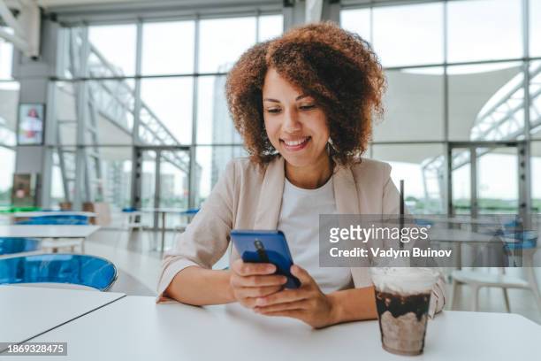 beautiful young woman using smartphone sitting in the cafe - café frappé fotografías e imágenes de stock