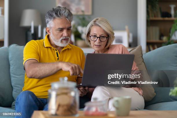 seniorenpaar sitzt zusammen auf dem sofa mit laptop - couple 50 55 laptop stock-fotos und bilder