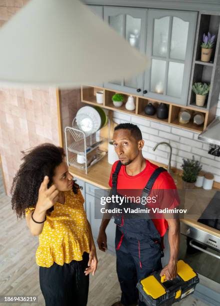 housewife looking at handyman while pointing up to the ceiling - handyman overalls stock pictures, royalty-free photos & images