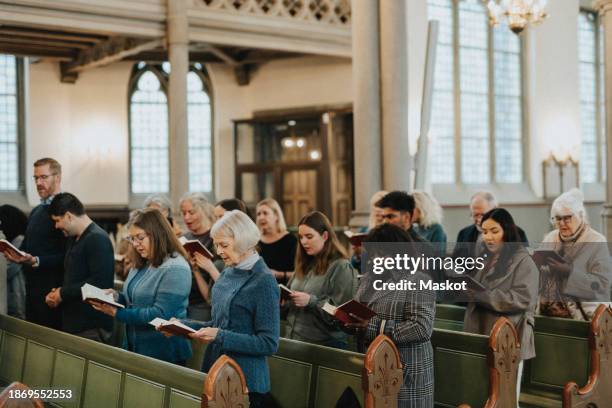 people reading hymnbook during mass at church - chiesa foto e immagini stock