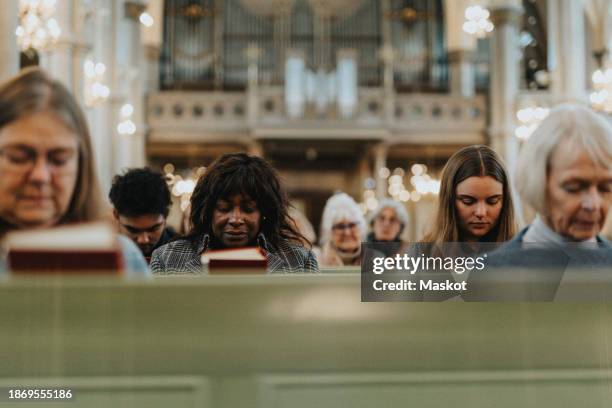 group of male and female protestants praying with eyes closed while sitting at church - female priest stock pictures, royalty-free photos & images