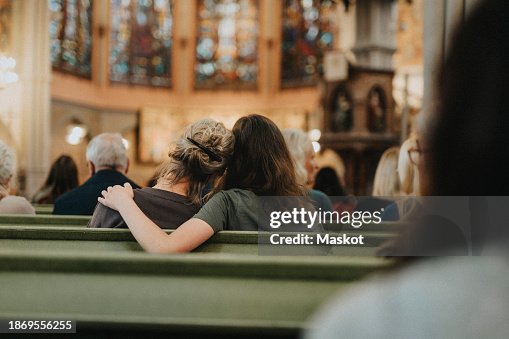 Teenage daughter sitting with arm around mother on bench at protestant church Teenage daughter sitting with arm around mother on bench at protestant church