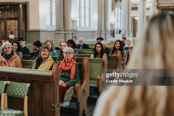 smiling male and female protestants sitting on pews while listening to priest at church - religious mass stock pictures, royalty-free photos & images