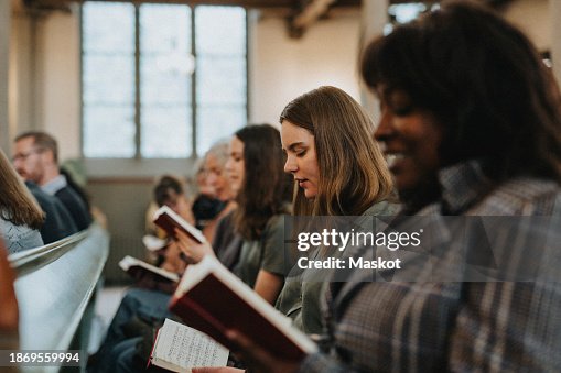 Young woman reading hymnbook while sitting with protestants at church