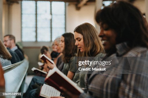 Young woman reading hymnbook while sitting with protestants at church Young woman reading hymnbook while sitting with protestants at church
