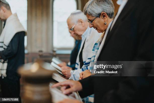 senior woman reciting amidah while standing during congregation at synagogue - reading synagogue stock pictures, royalty-free photos & images