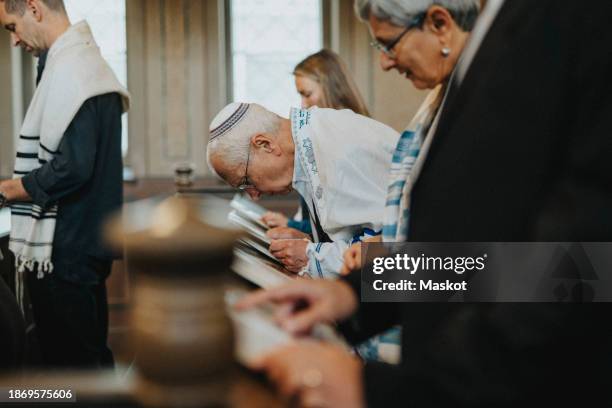 side view of senior man reciting amidah during jewish congregation at synagogue - juif photos et images de collection