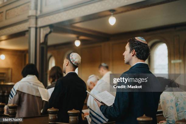 man wearing yarmulke and reciting amidah with people during jewish congregation at synagogue - jewish people stockfoto's en -beelden