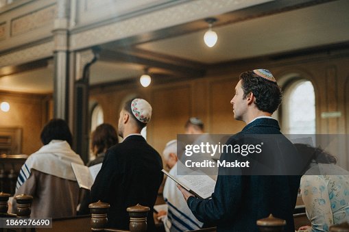 Man wearing yarmulke and reciting Amidah with people during Jewish congregation at synagogue