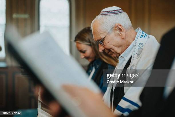 senior man wearing yarmulke while reciting amidah at jewish synagogue - jewish prayer shawl stock pictures, royalty-free photos & images