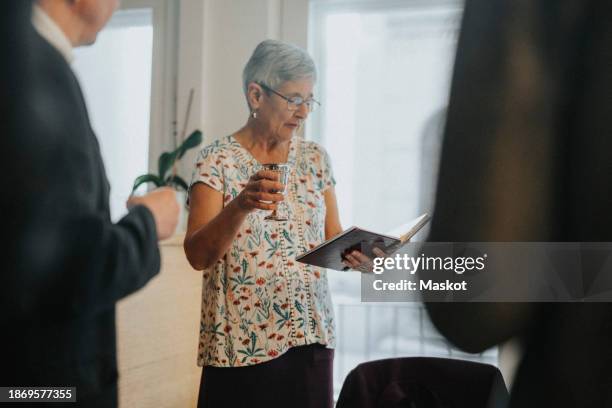 senior woman reading torah and toasting drinks during jewish congregation at synagogue - kiddush cup stock-fotos und bilder